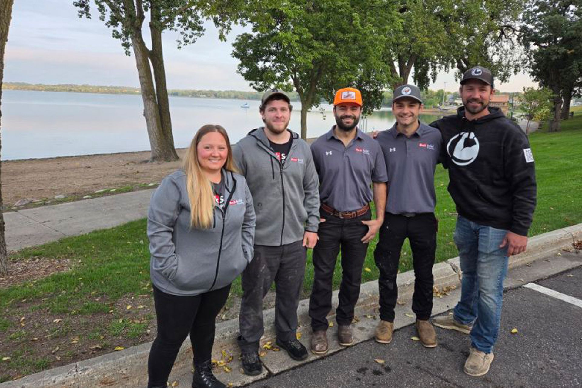 Five people in jackets stand by a lakeside path on a cloudy day.