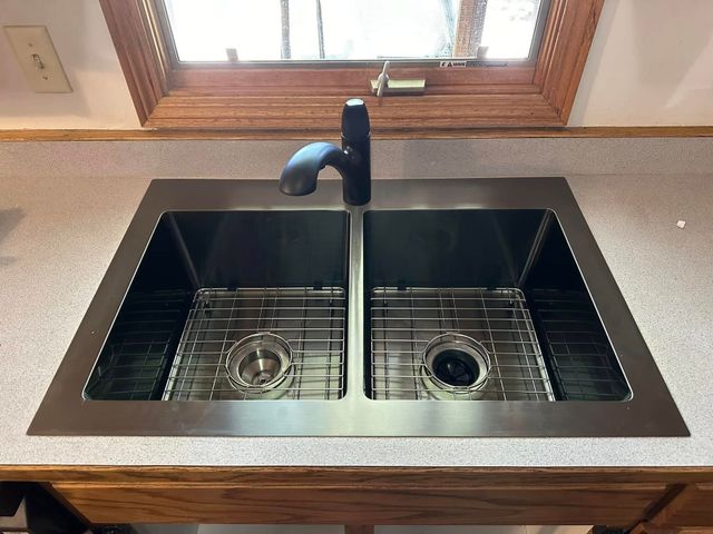 Black double-basin kitchen sink with matte black faucet beneath a window and wooden countertop.