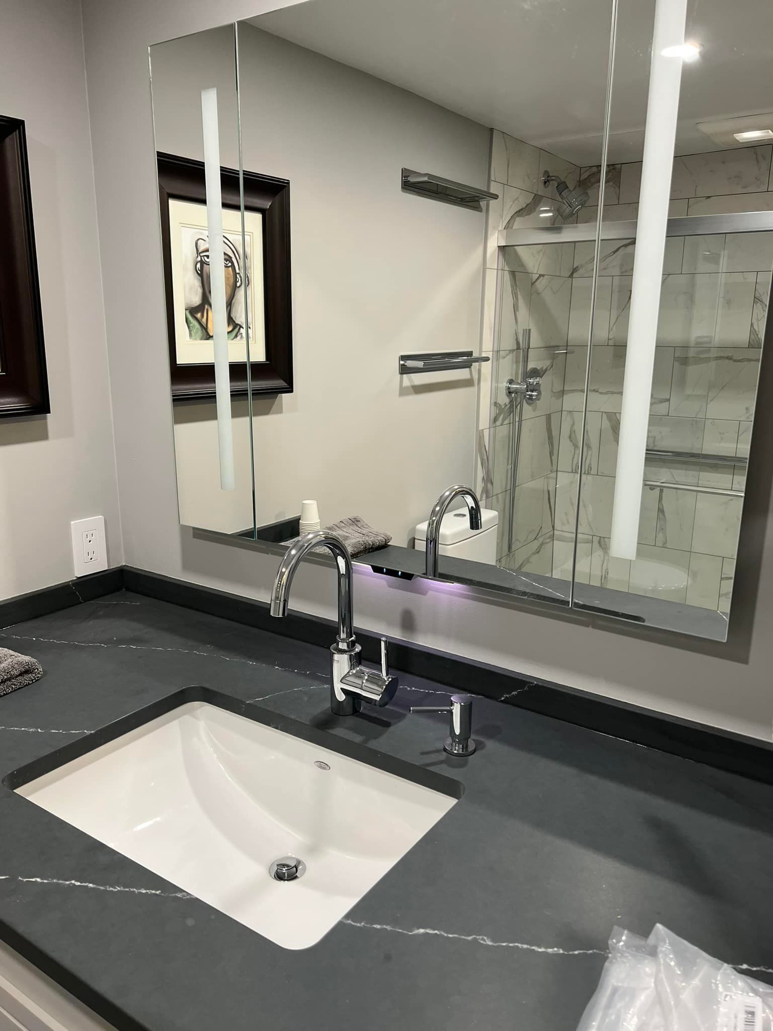 Bathroom sink with dark countertop, chrome faucet, and large mirror reflecting the room.