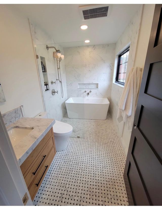 Modern white bathroom with mosaic tile floor, freestanding tub, vanity, toilet, and shower