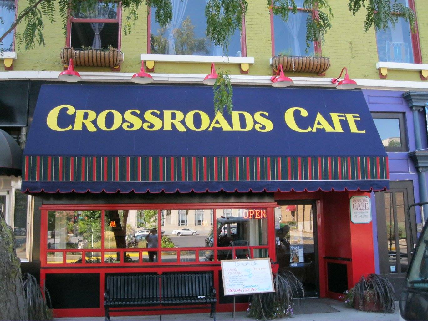 Crossroads Cafe storefront with blue awning, yellow text, red trim, and a black bench.