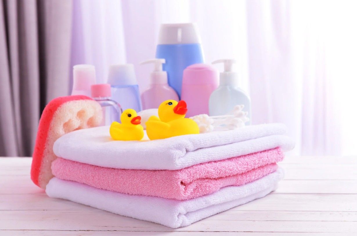 Stack of pink and white baby towels with rubber duckies and toiletries.