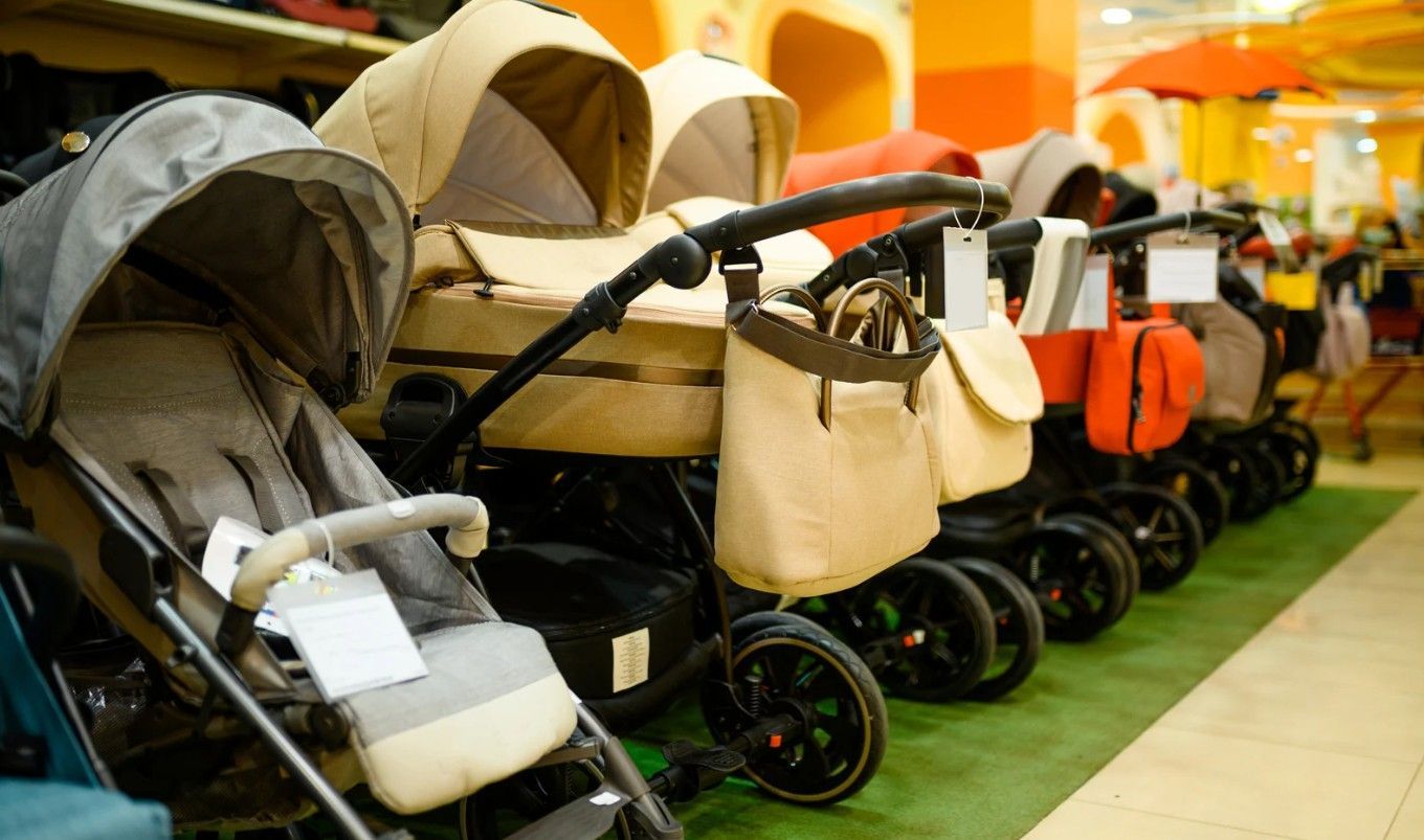 Row of strollers displayed in a store, beige and gray colors, wheels visible.