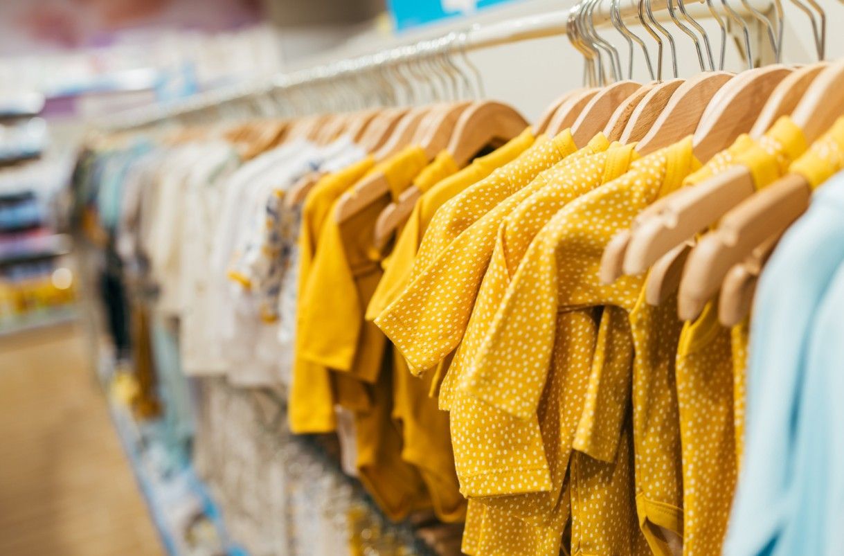 Clothes on hangers in a store, including yellow and white shirts.