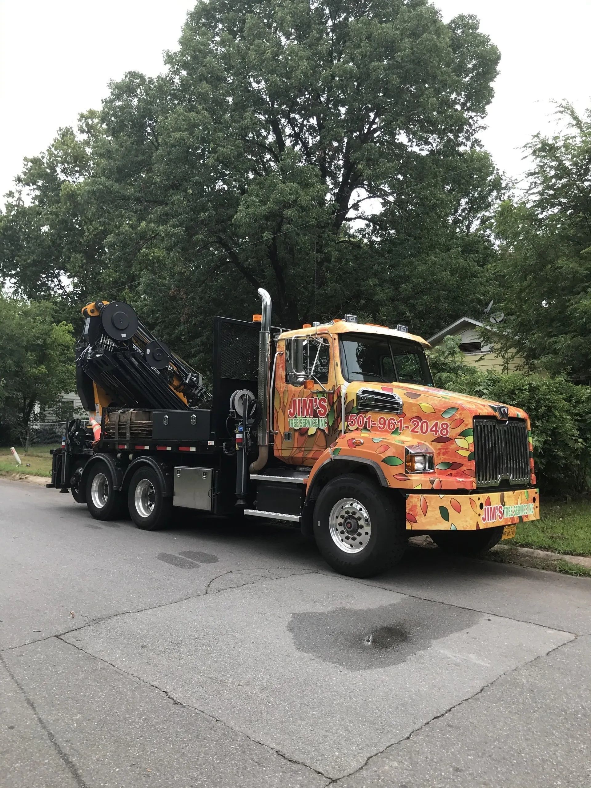 A yellow truck with a crane on the back is parked on the side of the road.