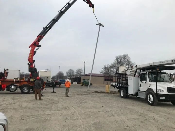 A crane is lifting a pole in a parking lot