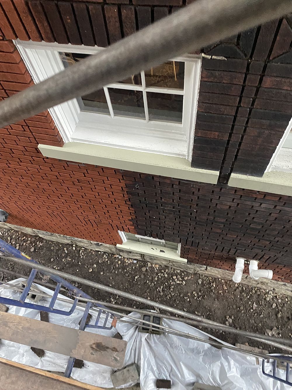 A brick building with a window is being painted.