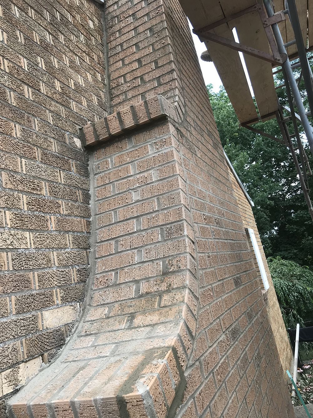 A brick chimney is being built on the side of a building.