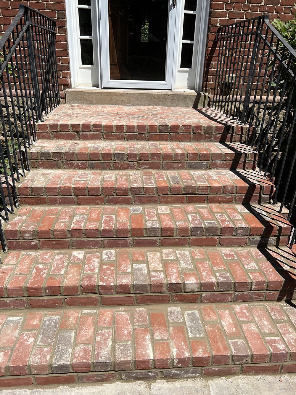 A set of brick stairs leading up to a house with a wrought iron railing.