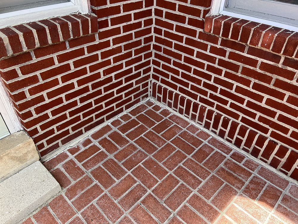 A corner of a brick wall with a tile floor.