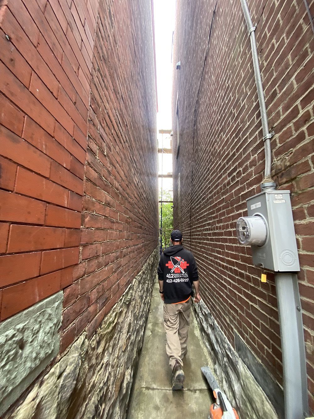 A man is walking down a narrow alleyway between two brick buildings.