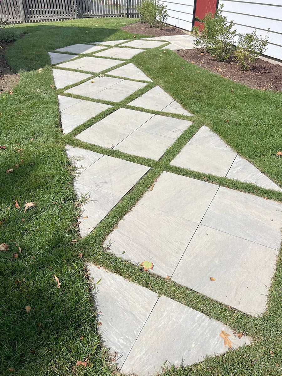 A concrete walkway surrounded by grass in front of a house