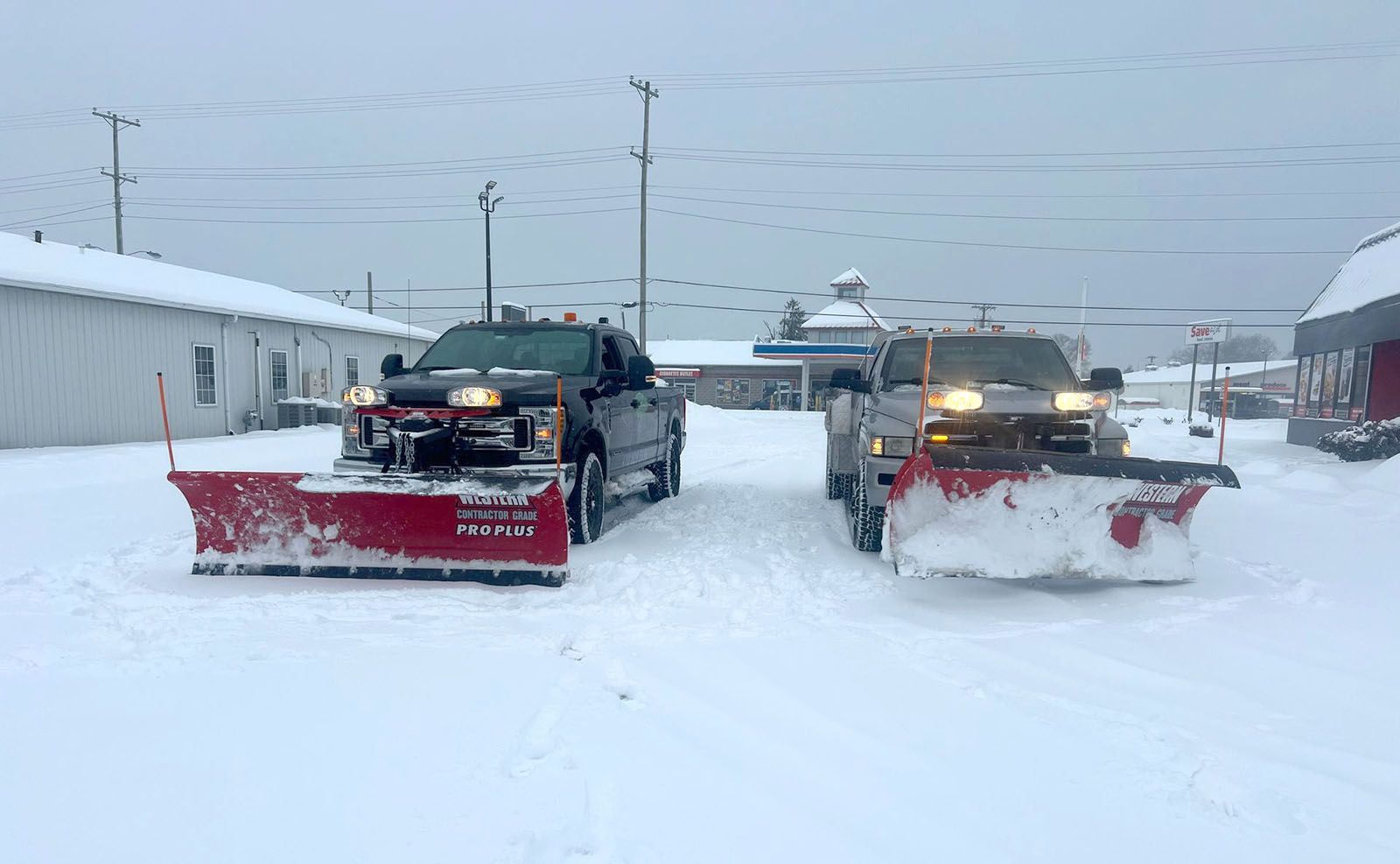 Two snow plowing trucks are parked next to each other in the snow