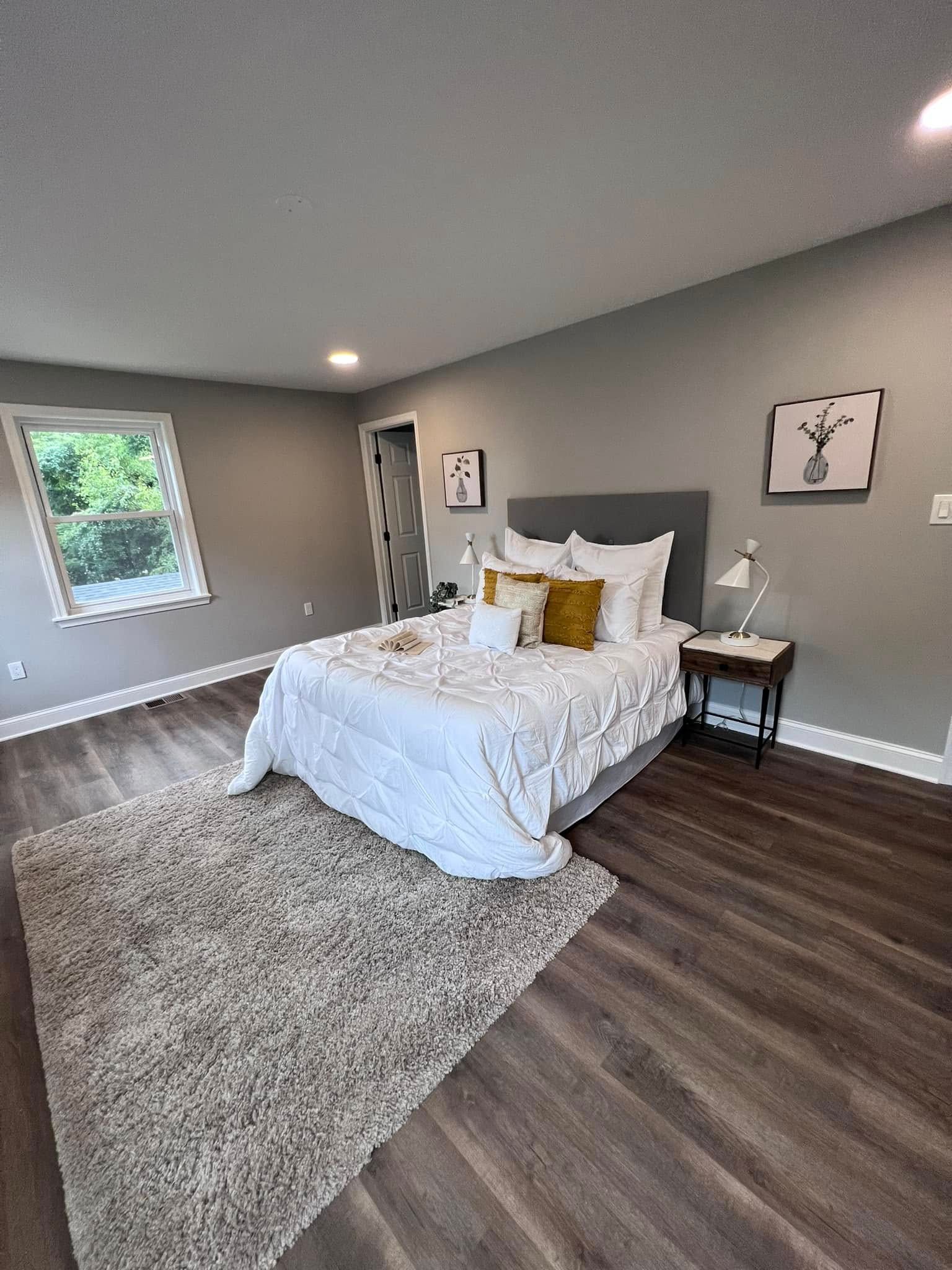 A bedroom with a bed , nightstand , rug and window.