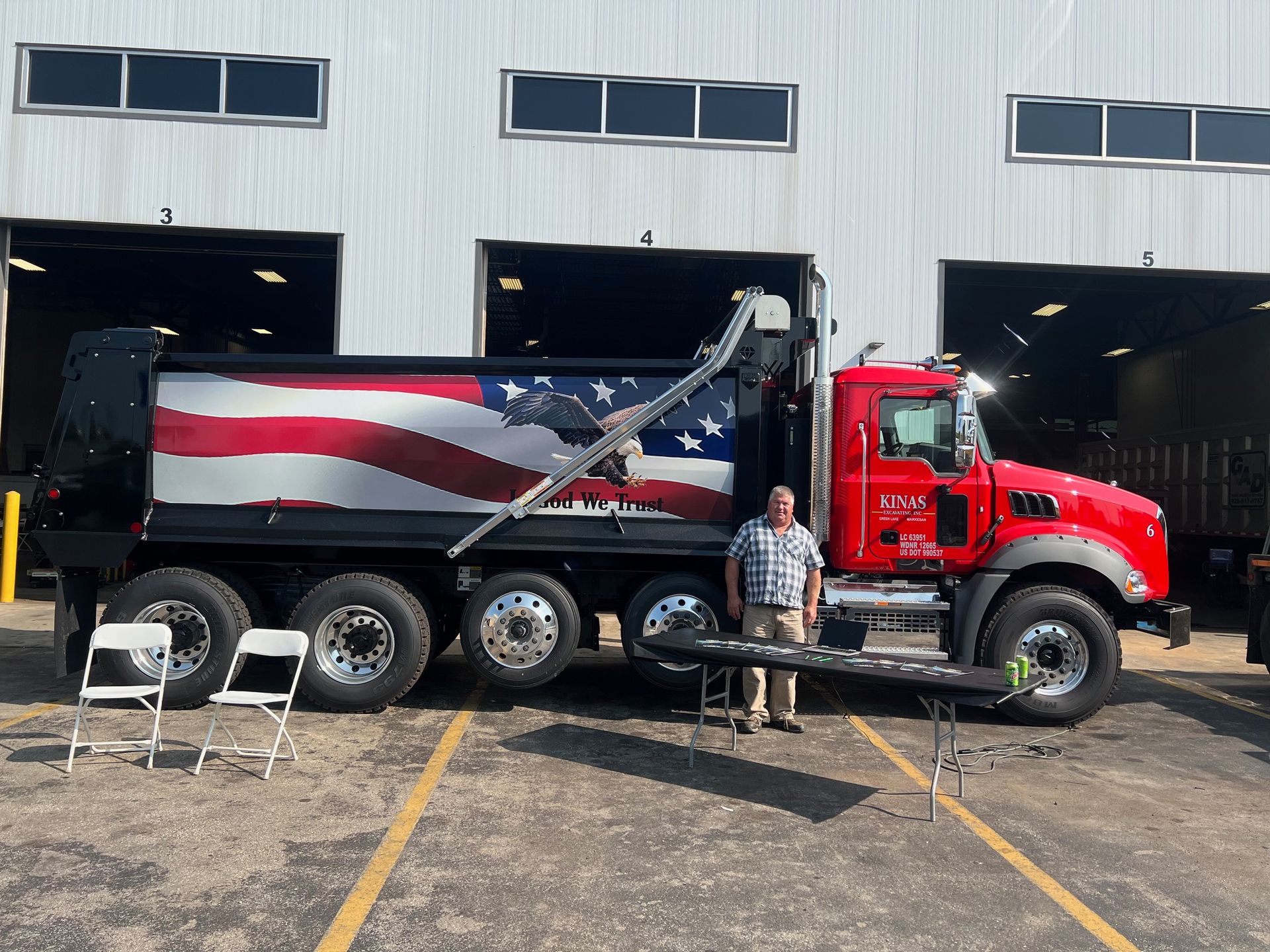 Red dump truck with American flag on the side, man standing next to it.