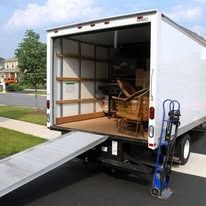 Moving truck with a ramp lowered, showing the open cargo area. A hand truck is next to the ramp.