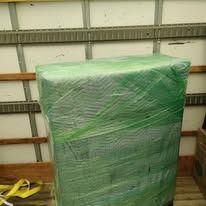 A large, rectangular item wrapped in green plastic wrap inside a truck or storage space.