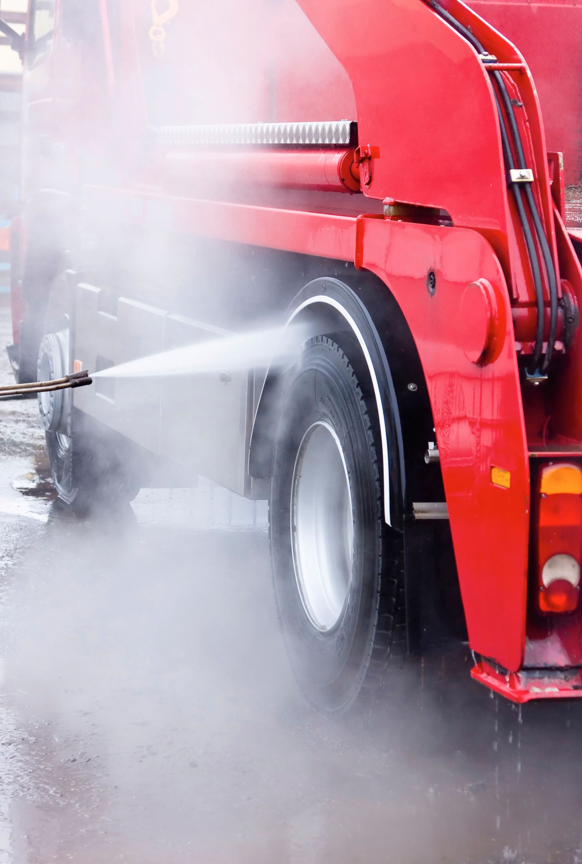 Red truck wheel being power washed, creating steam.