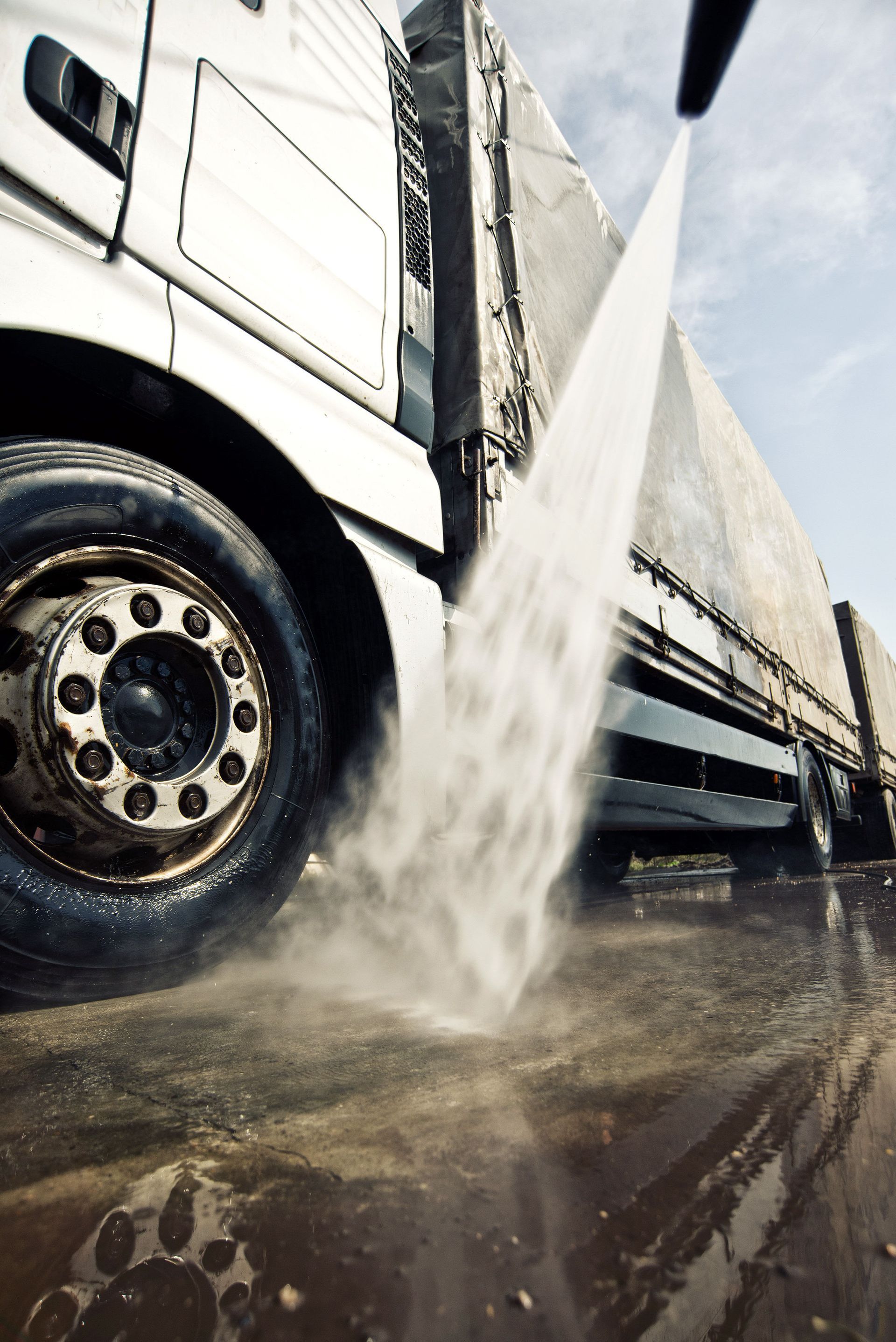 Pressure washing a semi-truck's side. Water sprays from the nozzle, cleaning the vehicle.