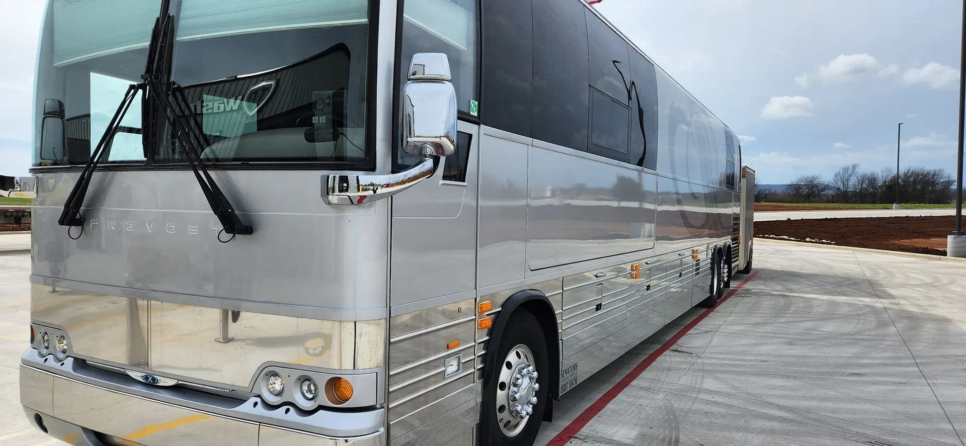 Silver tour bus parked on a concrete surface.