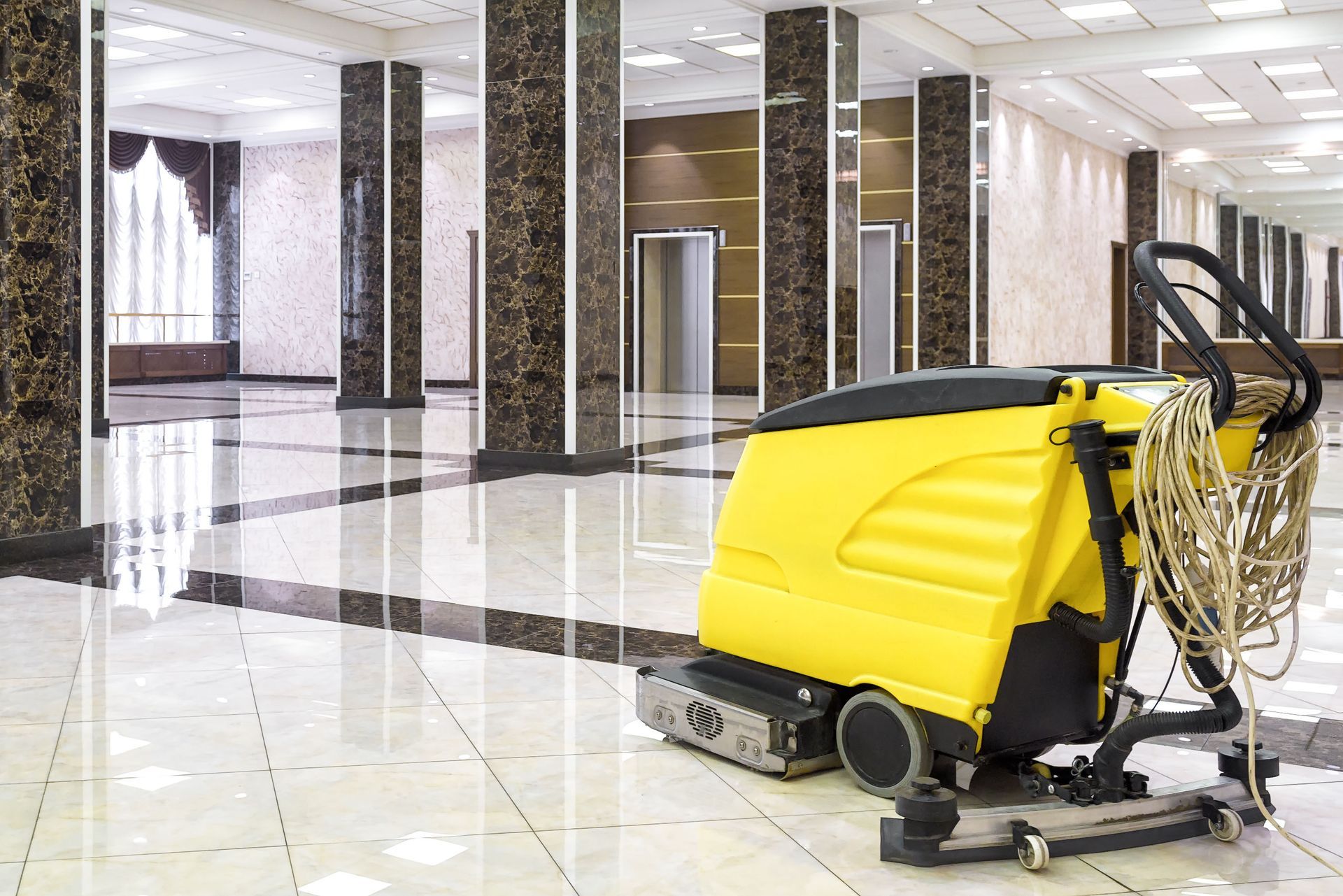 A yellow cleaning machine is sitting on a tiled floor in a large room