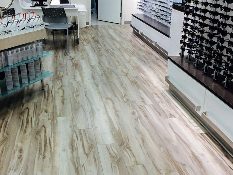 Optical store interior with wood-look flooring, eyeglasses displayed on shelves and counters.