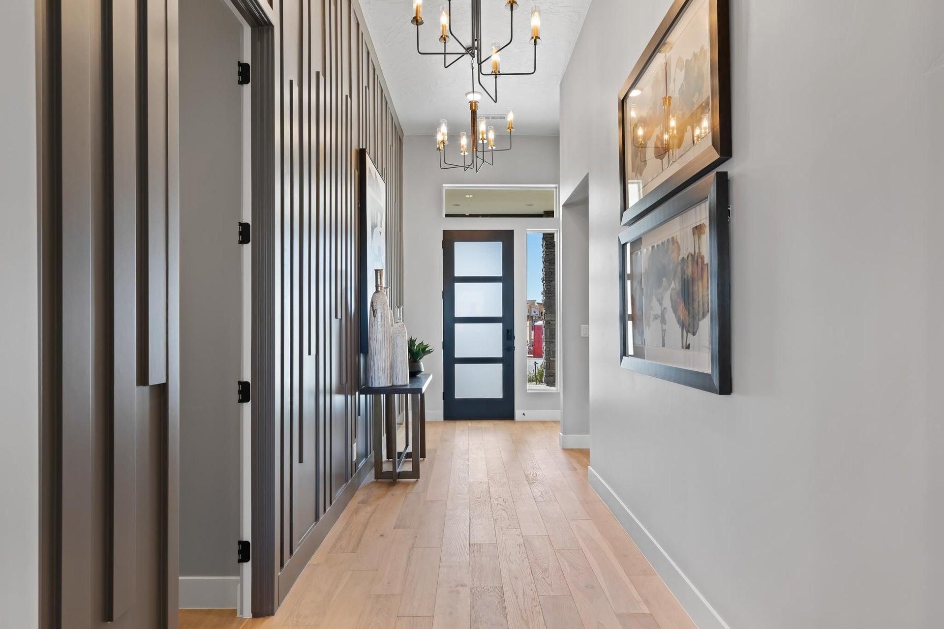 Hallway with wood flooring, grey walls, dark door, and artwork. Decorative paneling on one wall.