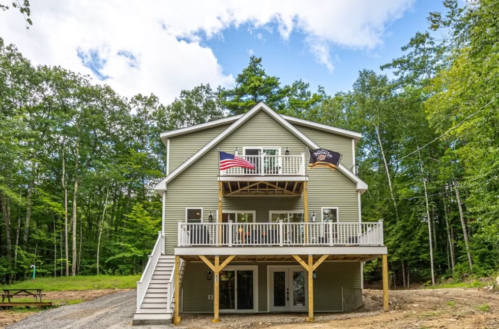 A large house with a large deck in the middle of a forest.