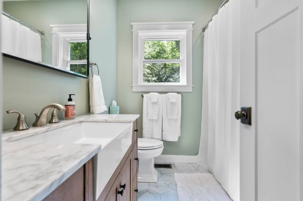 A bathroom with a sink, toilet, shower, and window.
