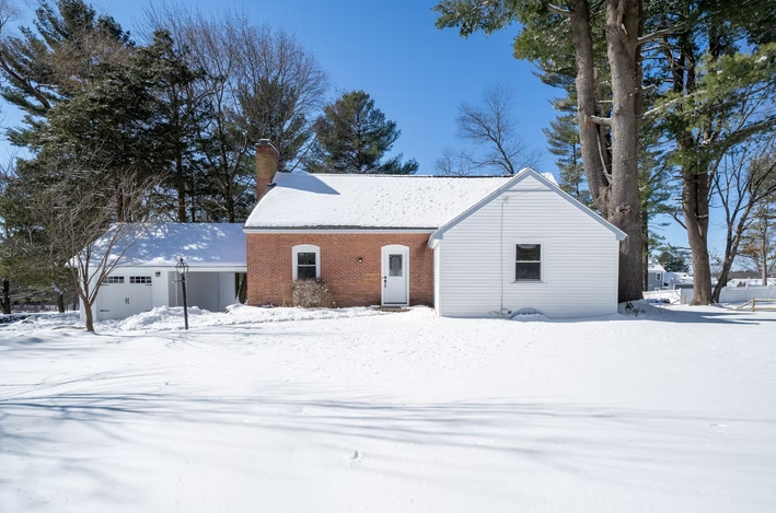 A small white house is sitting in the middle of a snow covered field.