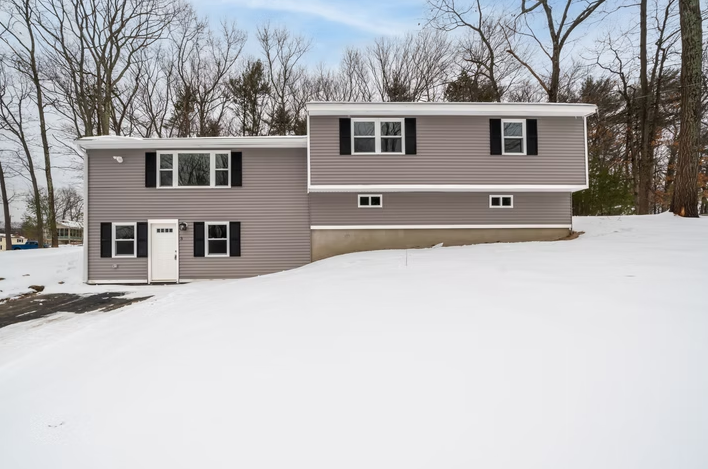 A house with a lot of snow on the ground and trees in the background.