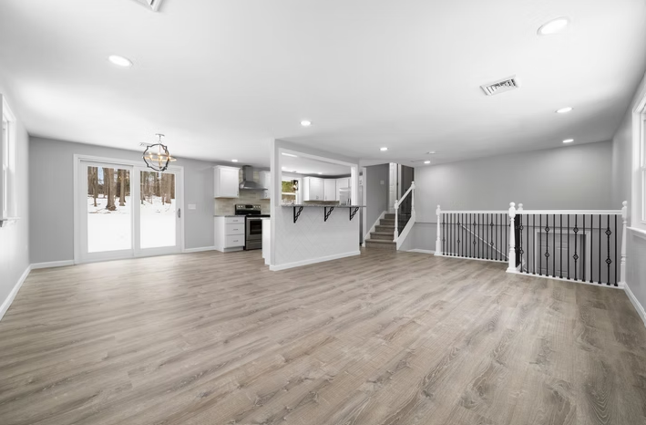 An empty living room with hardwood floors and a kitchen in the background.