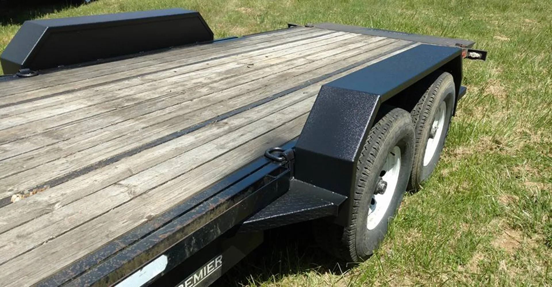 Black utility trailer with wooden deck and two tires.