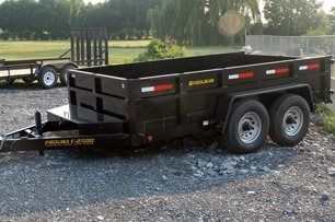 Black dump trailer on gravel, with two wheels, ready for hauling materials.