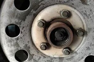 Close-up of a rusty car wheel hub with six bolts securing it to the wheel.