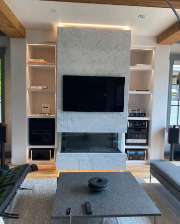Modern living room with a built-in fireplace, wall-mounted TV, and illuminated shelving units