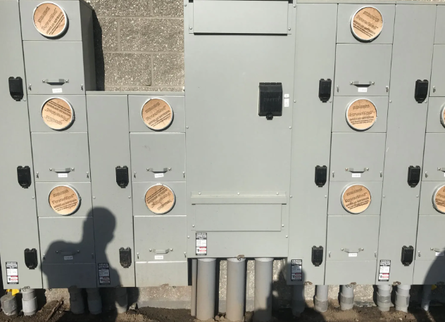 Gray electrical control cabinets outdoors with circular warning labels and a shadow in front