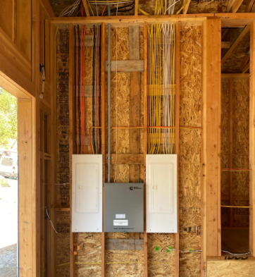 Electrical panel and wiring in an unfinished wooden wall with exposed studs and open boxes.