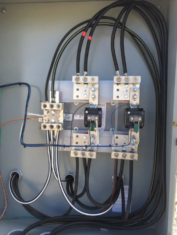 Electrical panel with wiring, relays, and circuit breakers mounted inside a gray cabinet.