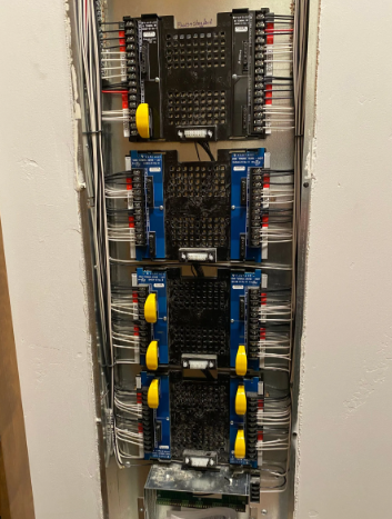 Vertical row of electronic control modules and wiring in a wall-mounted cabinet, with blue and black components.