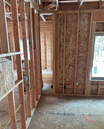 Unfinished house interior with exposed wooden framing, OSB walls, and a small window.