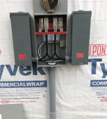 Open electrical meter panel with two gray boxes and exposed wiring mounted on a pole.