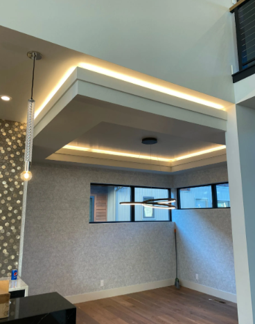 Modern empty room with a recessed ceiling, LED strip lighting, and windows on two walls.