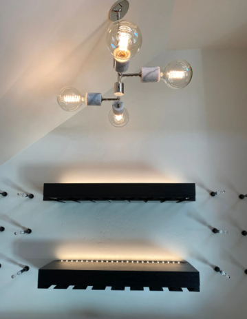 Modern wall display with two sleek black shelves and ceiling light fixture against white walls