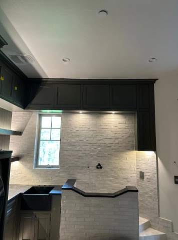 Modern kitchen alcove with black cabinets, white brick backsplash, and a small window above a sink area