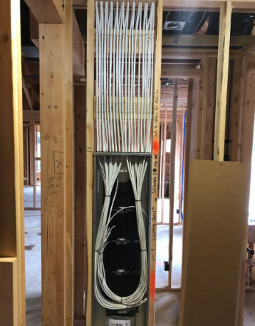 Unfinished wall framing with bundled white cables and a black electrical box in a house under construction