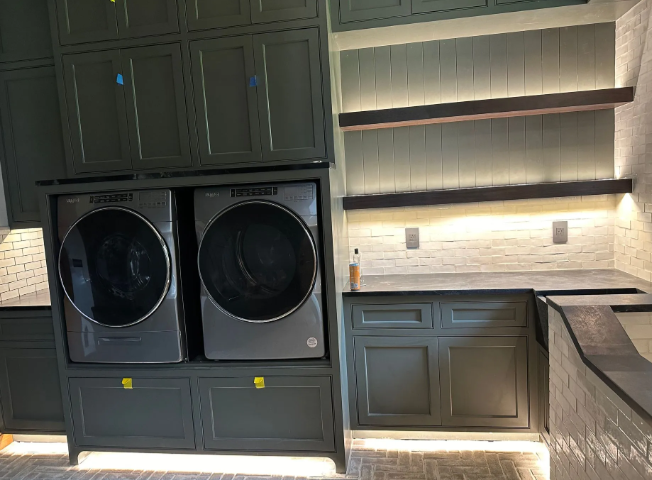Built-in laundry room with stacked washer and dryer, gray cabinets, open shelves, and warm under-cabinet lighting