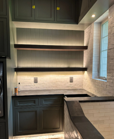 Modern kitchen nook with dark cabinets, open shelves, marble backsplash, and a window on the right