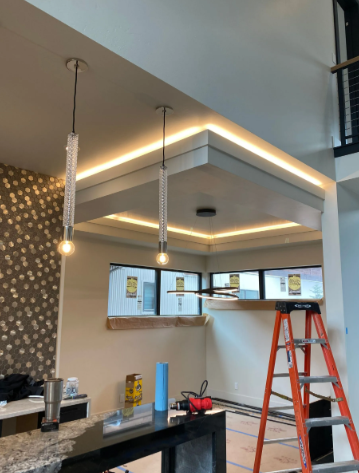 Interior remodel with ceiling soffit lighting, hanging pendant lights, and a red ladder in a kitchen area