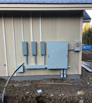 Utility meters and electrical boxes mounted on a beige building exterior next to a dirt trench